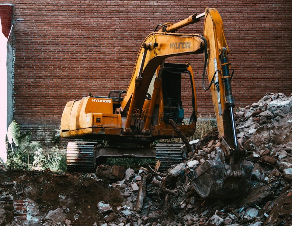 yellow excavator beside brown brick wall